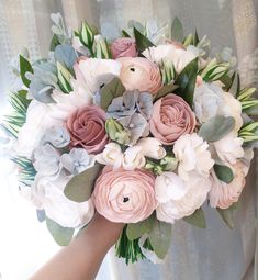 a bridal bouquet with pink, white and blue flowers is held by a woman's hand