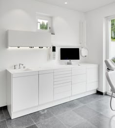 a modern kitchen with white cabinets and black flooring, along with a large flat screen tv mounted on the wall