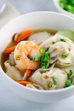 a white bowl filled with shrimp and dumplings on top of a table next to chopsticks