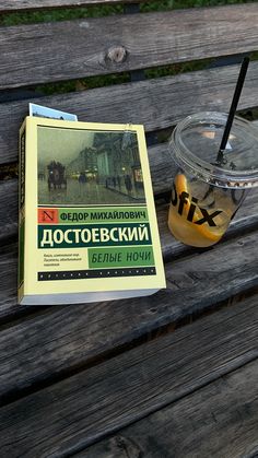 a book sitting on top of a wooden bench next to a cup filled with liquid