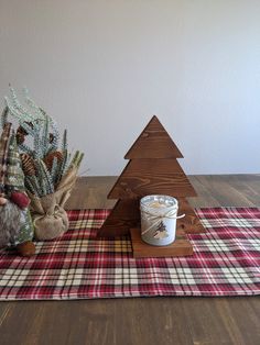 a small wooden christmas tree next to a cup of coffee on a plaid tablecloth