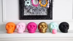 there are five different colored skulls sitting on the mantle in front of a framed photo