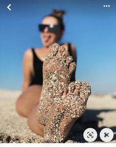 a woman laying on top of a sandy beach next to the ocean with her feet covered in sand