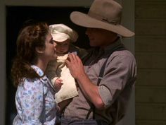 a man holding a baby in his arms while standing next to a woman wearing a cowboy hat