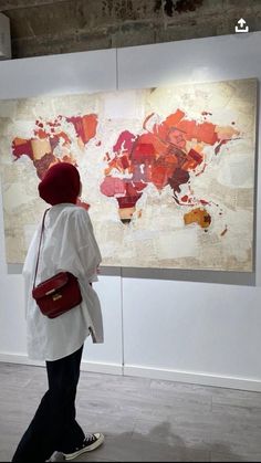 a woman walking past a large map in an art gallery with red and white colors