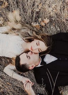 a man and woman laying on the ground in tall grass with their heads touching each other