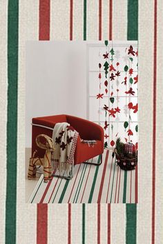 a red couch sitting on top of a wooden floor next to a window covered in christmas decorations