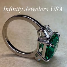 "-Approximate total carat weight: approx. 6.00ctw diamond equivalent #7080 -Center Stone Size: 11x9mm - approx. 4.90ct diamond equivalent -Center Stone Shape: emerald cut -Gem Type: lab created Green Emerald -Stone Clarity: VS2 -Stone Color: F -Moh's Scale: 9 hardness -Side Stones Size: 6x4mm trapezoid approx. 0.55ct. each diamond equivalent -Gem Type: Zonar moissanite -Metal Type and Purity: 14k white gold -Setting: 4 prong tulip setting -Stock Ring Size: 5.75 -Country of Manufacturing: USA (Mi Luxury Green Heart Cut Rings, Green Diamond Platinum Ring With Prong Setting, Green Gemstone Platinum Ring, Platinum Green Ring For Anniversary, Platinum Green Gemstone Rings, Green Platinum Anniversary Rings, Platinum Green Rings For Anniversary, Gia Certified Trillion Cut Emerald Rings, Green Platinum Ring For May Birthstone