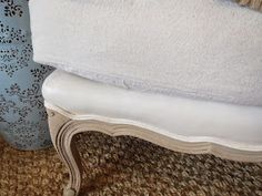 a white bench sitting next to a blue vase on top of a carpeted floor