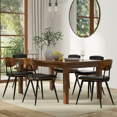 a dining room table with four chairs and a round mirror on the wall above it