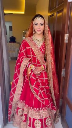 a woman in a red and gold bridal gown posing for the camera with her hands on her hips