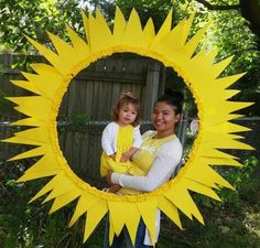 a woman holding a child in front of a sunflower frame