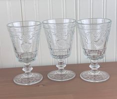 three clear glass goblets sitting on top of a wooden table next to each other