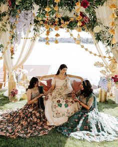 three women sitting on a couch in front of a flower covered arch with flowers hanging from it