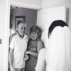 an older man and woman standing in front of a mirror looking at each other's reflection