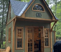 a small green building with a blue roof and two wooden chairs in front of it