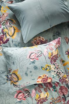 the comforter is made up with blue sheets and floral print on it, along with two pillows