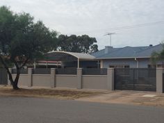 a grey house with a tree in the foreground and a fenced off area behind it