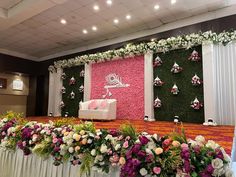 a decorated stage with flowers and greenery on the wall, in front of a white couch