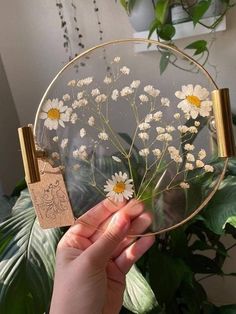 a person holding up a glass plate with flowers on it in front of a potted plant