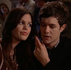 a young man and woman are looking at their cell phones while sitting in a restaurant