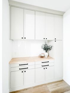 an empty kitchen with white cabinets and wood counter tops, along with a potted plant