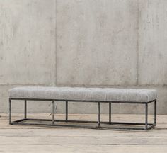 a bench sitting on top of a wooden floor next to a cement wall with a metal frame