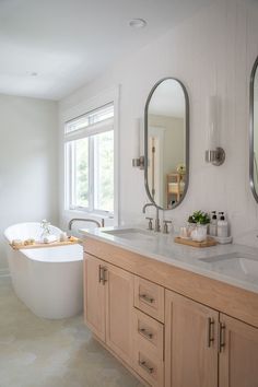 a large white bath tub sitting next to two sinks in a bathroom with mirrors on the wall