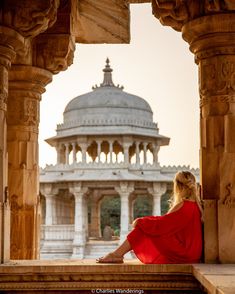 a woman in a red dress is sitting on steps looking out at the building behind her