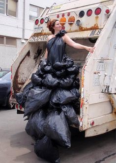 a woman in a black dress standing next to a garbage truck with bags on the back