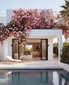 the pool is surrounded by pink flowers and greenery on the side of the house