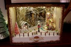 a christmas scene is displayed in a frame with lights and snow on the ground next to trees