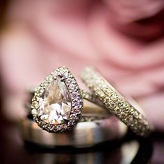 two wedding rings with diamonds on them sitting on top of a black table in front of a pink rose