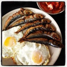 fried fish and eggs on a plate with tomatoes