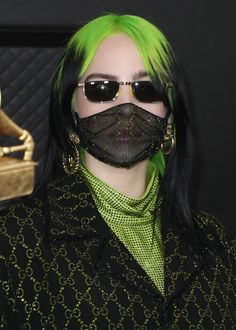 a woman with green hair wearing a black face mask and gold hoop earrings