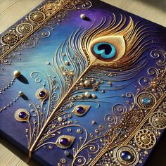 a blue and gold painted canvas with a peacock's feather on it, sitting on a table