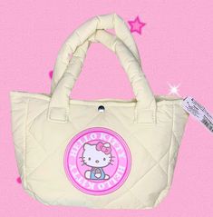 Sanrio Hello Kitty Puffer Tote Womens Puffy Quilted BagHello Kitty is back with this Sanrio Hello Kitty Puffer Tote Bag! This versatile, lightweight, everyday bag, is equal parts practical and stylish! Quilted design filled with down pockets, giving it a "puffer jacket" appearance. Effortlessly casual, but not boring, the white textured exterior has KT in a large circle pink patch front and center, with a smaller leather pink patch with "Hello Kitty" Sanrio on the back. Handle will slip right over you shoulder with ease, made of the same smooth puffer material. Large enough for all your daily essentials, the medium sized bag gradually expands slightly from top to bottom. Simple snap closure secures in a quick and easy fashion! Seamlessly Kawaii with comfort, this bag will bring you KT's gi Puffer Tote Bag, Pink Patch, Easy Fashion, Hello Kitty Sanrio, Womens Bag, Medium Sized Bags, Daily Essentials, Everyday Bag, Quilting Designs