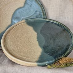 two blue and beige plates sitting on top of a white cloth covered tablecloth next to a pine cone