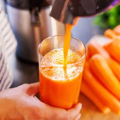 a person is pouring orange juice into a glass with carrots in front of them