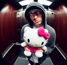 a man in a hoodie holding a hello kitty stuffed animal while looking at the camera