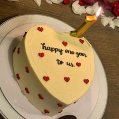 a heart shaped cake with the words happy one year to us written on it and lit by a candle