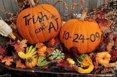 two pumpkins with writing on them sitting in front of some autumn leaves and flowers