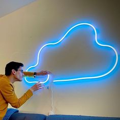 a man sitting on a couch in front of a cloud shaped neon sign that is hanging from the wall