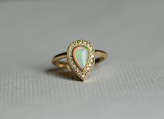 an opal and diamond ring sits on a table with a white surface in the background