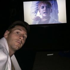 a man sitting in front of a tv with a woman on the screen behind him