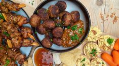 two plates with meatballs and carrots next to other foods on a wooden table