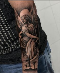 a man with a tattoo on his arm holding an angel and cross in the background