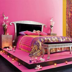 a bedroom with pink walls and purple carpeted flooring, lit by candles on either side of the bed