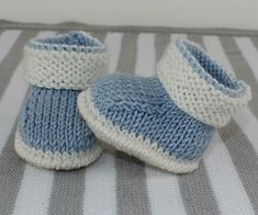 two blue and white knitted baby booties sitting on top of a striped blanket