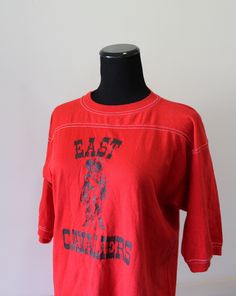 Here we have a great Vintage East Cavaliers Graphic T-Shirt from the 1970s. The tag is missing but I believe it is made of 50% cotton, 50% polyester and it is a size large. On the front of this red shirt is a cavalier and it reads EAST CAVALIERS in black. The shirt measures 20 inches from pit to pit and 29 inches in length. It is in good shape and broken in nicely, there are two small stains on the back shoulder (photo 6). This cool shirt would add a retro pop to any outfit! Retro Red T-shirt With Screen Print, Red Retro Top With Graphic Print, Vintage College T-shirt With Graphic Print, Vintage College T-shirt With Screen Print, American Retro Short Sleeve Cotton T-shirt, American Retro Cotton Tops With Screen Print, Retro Red College Tops, Vintage Cotton T-shirt For College, Vintage Screen Print Tops For College